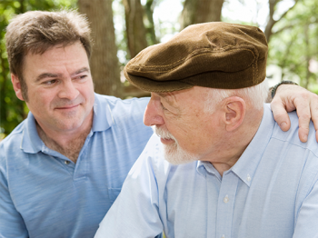 Man putting his arm around his elderly father in the park