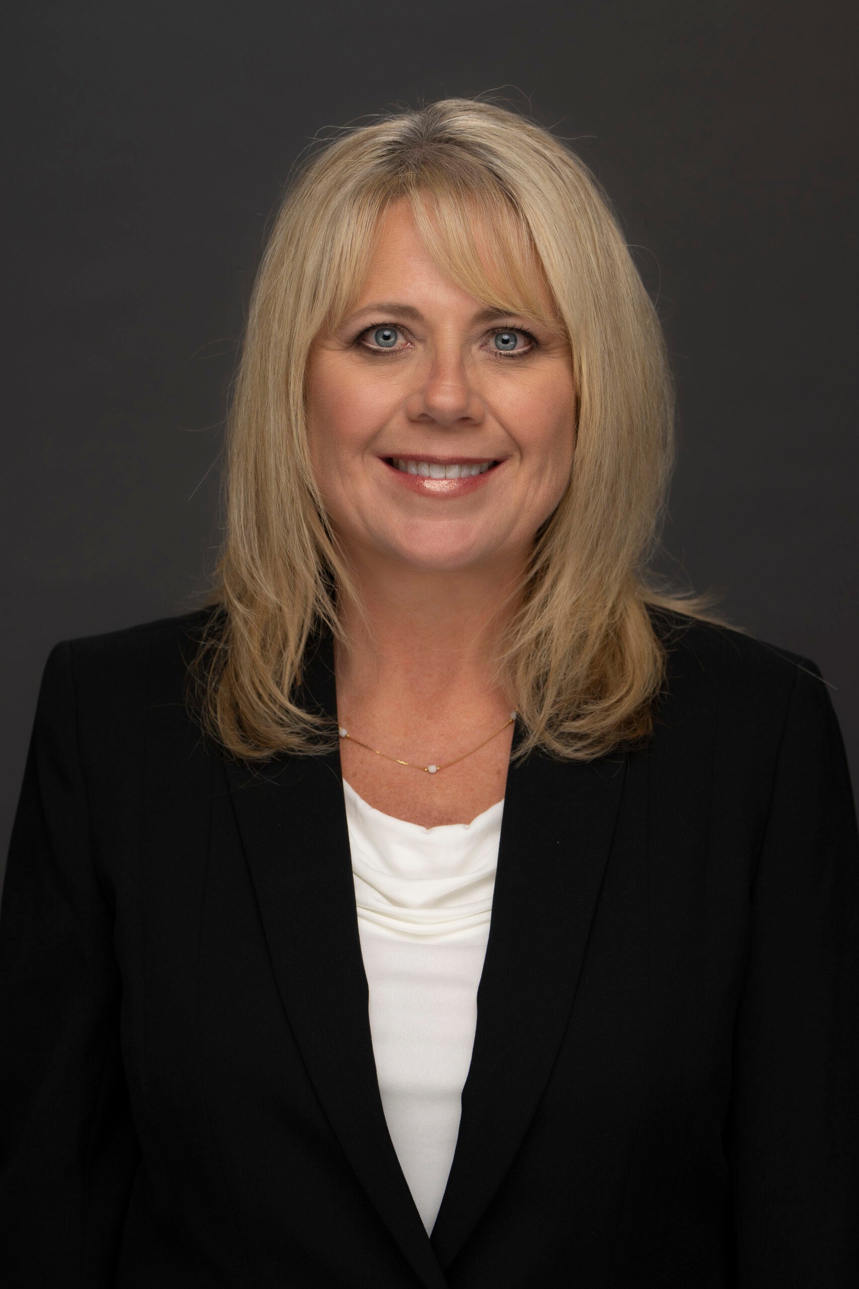 Head-and-shoulders portrait of Carol Cox wearing a black blazer and white blouse against a dark background.
