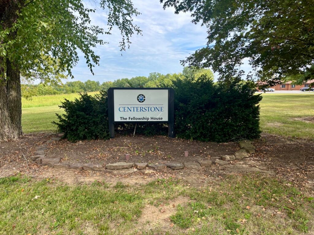 Centerstone Fellowship House sign amid shrubs and trees on a grassy campus.
