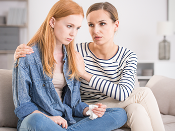 Concerned mother putting her arm around troubled teen daughter