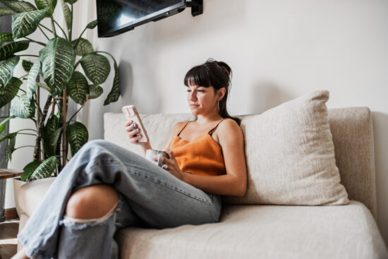 Young woman using mobile phone sitting on sofa at home