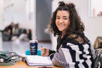 girl with dark hair sitting at desk smiling toward camera