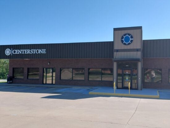Exterior of a brick Centerstone building with signage, glass entrance doors, and yellow safety bollards.