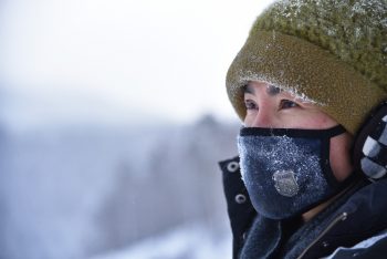 woman wearing green knit cap and blue mask in snow