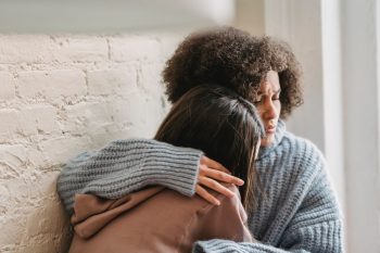 one woman in blue comforting a woman in light red