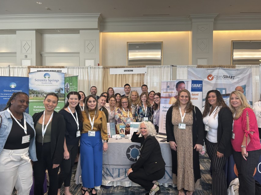 A large group of staff gather around a Centerstone booth at an event in Florida for a photo.