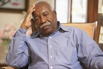 Older depressed looking man sitting in a chair in his living room alone.