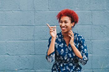 black woman with red hair in front of blue wall smiling and pointing