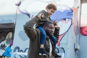 man holding son on his shoulders walking on the street