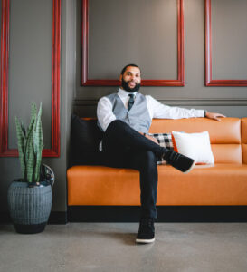 man wearing suit sitting on orange couch in room with gray walls