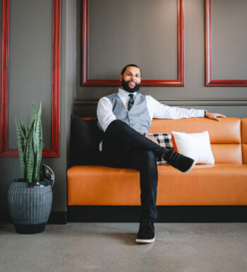 man wearing suit sitting on orange couch in room with gray walls