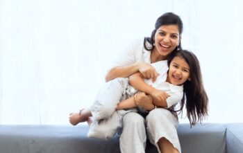 mother holding daughter sitting on gray couch wearing white, smiling