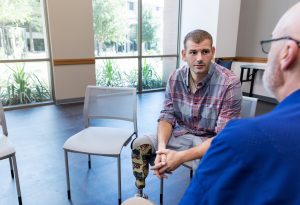 Mid adult veteran with prosthetic leg, listens to unrecognizable therapist