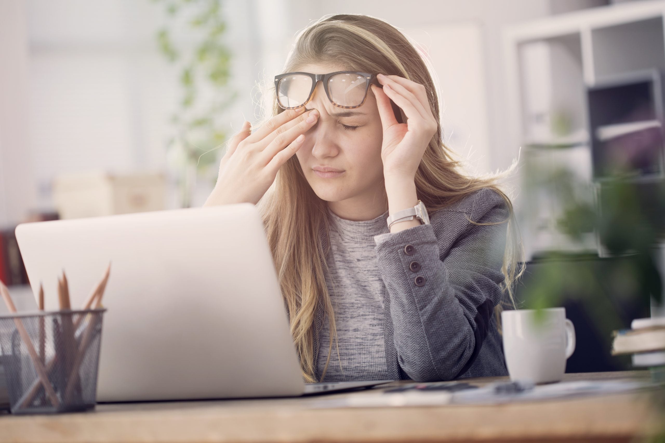 woman sitting at desk and rubbing head to soothe tension headache
