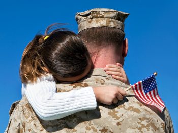 Soldier in fatigues ready for deployment hugging daughter with american flag