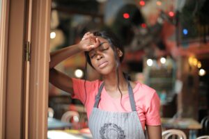 woman wearing pink shirt and gray apron leaning on brown doorway