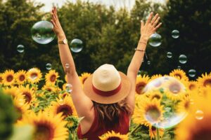 woman standing in sunflower field with arms raised and bubbles around