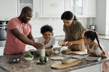 parents and children standing around kitchen island preparing food