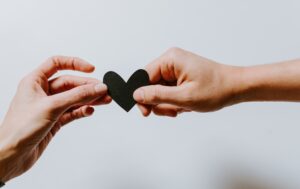 two people's hands holding black paper cutout heart