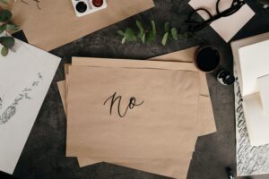piece of brown paper reading "no" sitting on black table surrounding by other papers