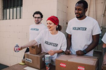 three people standing behind table with medical supplies wearing volunteer shirts