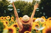 woman standing in sunflower field with arms raised and bubbles around