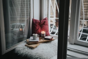 pillow, candle, mug and book on a wooden tray sitting in the window